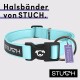 Ein hellblauer Hundehalsband mit einer schwarzen Schnalle, die ein Hundelogo zeigt, beschriftet mit "Halsbänder von STUCH." und einem Etikett mit der Aufschrift "PETA APPROVED VEGAN."