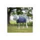 Ein graues Pferd, das eine marineblaue gepolsterte Decke trägt, steht auf grünem Gras, umgeben von Bäumen und einem Zaun im Hintergrund.