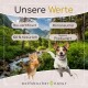 Ein verspielter Hund und eine Katze in einer grünen Landschaft mit einem Bach. Der Text zeigt "Bio-zertifiziert", "Klimaneutral" und "Regional Produziert."
