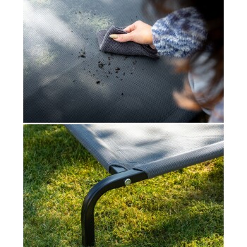 Eine Person, die ein graues Haustierbett mit einem Tuch reinigt, wobei Schmutz auf dem Stoff zu sehen ist, mit einer Nahaufnahme des Metallrahmens des Bettes auf Gras.