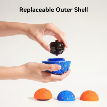 Eine Hand legt einen schwarzen Ball auf eine blau-orange strukturierte Schale, mit drei bunten Schalen darunter. Text: "Austauschbare äußere Schale."