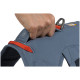 Eine Nahaufnahme einer Hand, die den Griff eines blauen Hundegeschirrs hält, mit einem orangefarbenen Riemen und einem reflektierenden Anhänger.