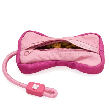 Pinkes, knochenförmiges Hundespielzeug mit Reißverschluss, gefüllt mit Trockenfutter, mit angebrachtem pinken Band und quadratischem Anhänger mit weißem Logo/Text.