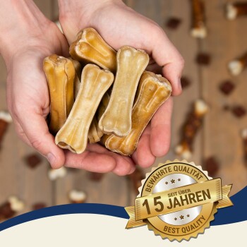 Ein Paar Hände, die mehrere hundeknochenförmige Leckerlis halten, mit einem Abzeichen, das "15 Jahre" und "Beste Qualität" auf Deutsch angibt.