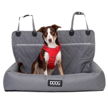 Ein brauner und weißer Hund mit einem roten Geschirr sitzt auf einem grauen Haustiersitzbezug mit einem gesteppten Design, mit dem Markenlogo "DOOG."