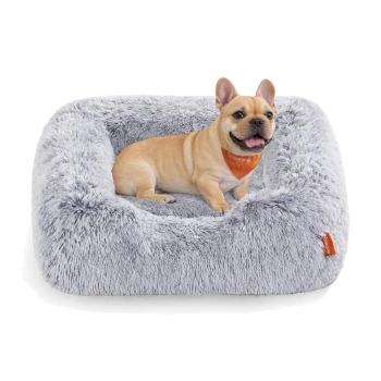 Ein hellgraues, plüschiges Hundebett mit einem kleinen tanfarbenen Hund, der darin sitzt und ein oranges Halstuch trägt.