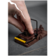 Eine Hand stellt eine braune Mausefalle mit einem gelben Hebel auf einer grauen Oberfläche ein.