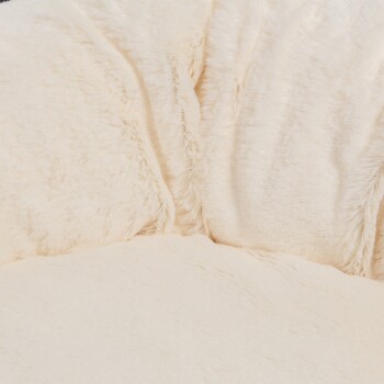 Ein plüschiges, cremefarbenes Haustierbett mit einer weichen, flauschigen Textur, das ein abgerundetes Design und ein gemütliches Aussehen aufweist.