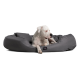 Ein weißer Hund, der auf einem grauen Haustierbett mit weichem, abgerundetem Design liegt, mit einem kleinen schwarzen Logo an der Seite.