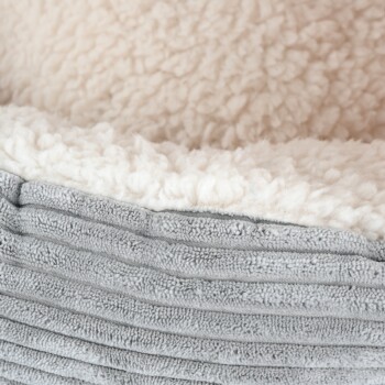 Nahaufnahme eines weichen, plüschigen Haustierbettes mit einem flauschigen cremefarbenen Innenraum und einer strukturierten grauen Außenseite.