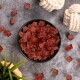 Eine schwarze Schüssel gefüllt mit kleinen, gewürfelten roten Haustierleckereien, umgeben von verstreuten Stücken und zwei geknoteten Seilspielzeugen auf einer grauen Oberfläche.