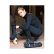 Eine Person in schwarzer Sportkleidung zieht einem Pferd einen Schutzstiefel über das Bein, während ein weiterer gerollter Stiefel auf dem Boden sichtbar ist.