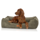 Ein brauner Irish Setter Hund, der bequem in einem grünen Cord-Haustierbett mit einem Lederschild, das "KNUFFELMUZ" liest, entspannt.