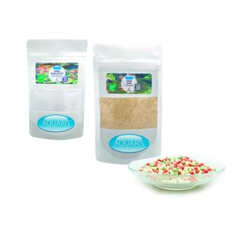 Zwei Beutel Aquaris Fischfutter, einer mit bunten Flocken und der andere mit einem beigen Pulver, neben einem Teller mit mehrfarbigen Pellets.