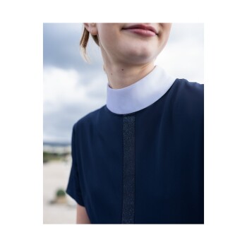 Nahaufnahme einer Person in einem marineblauen Kleid mit weißem Kragen und einem glitzernden vertikalen Streifen auf der Vorderseite, vor einem bewölkten Himmel.