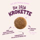 Runde Tierkrokette mit deutschem Text 'Die 2026 KROKETTE', 'Neue Größe: Jetzt auch in klein', 'Mit frischem Fleisch'.