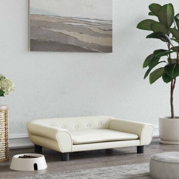 Ein stilvolles, cremefarbenes Haustierbett mit gepolsterten Knöpfen steht auf einem Holzboden, neben einer weißen Futterschüssel, die mit Trockenfutter gefüllt ist, und einer Topfpflanze.