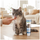 Grau getigertes Kätzchen leckt ein Leckerli von einer Hand neben einer Tube mit der Aufschrift 'SUPPORT OPTIMIZE & CARE' und einer Abbildung von Katze und Hund