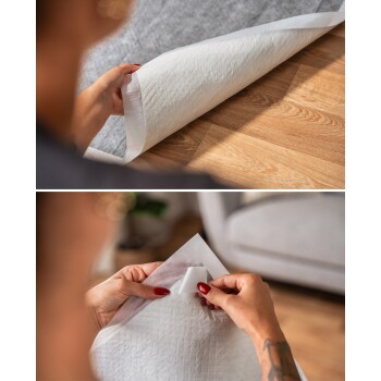 Eine Person mit roten Nägeln, die ein weißes Haustier-Trainingspad mit einer strukturierten Oberfläche ausrollt, um es auf einem Holzboden zu platzieren.