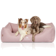 Zwei Hunde, die zusammen auf einem weichen rosa Haustierbett liegen, mit dem Logo 'KNUFFELWUFF', das auf der Vorderseite sichtbar ist.