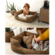 Ein braunes Hundebett mit einem weichen, plüschigen Innenraum, mit einem Hund, der darin sitzt. Eine Hand passt den Stoff des Bettes an.