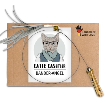 Ein handgemachtes Haustierzubehör-Paket mit einem kreisförmigen Draht mit einem Holzgriff, beschriftet mit "KATER KASIMIR BÄNDER-ANGEL," auf einem braunen Hintergrund.