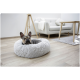 Ein Französischer Bulldogge ruht in einem flauschigen grauen Haustierbett, mit einem modernen Wohnzimmer im Hintergrund, das ein helles Sofa und einen Holztisch zeigt.
