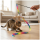 Getigerte Katze geduckt auf Parkettboden, die ein Regenbogenband-Spielzeug an einem von einer Hand gehaltenen Stab in einem Wohnzimmer anpirscht.