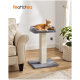 Ein gemütlicher Katzenbaum mit einer grauen und cremefarbenen Farbgebung, der eine plüschige obere Liegefläche und ein baumelndes Pom-Pom-Spielzeug hat, steht neben einem beigen Sofa.