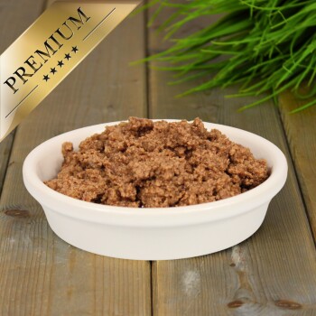 Eine weiße Schüssel gefüllt mit hochwertigem Haustierfutter, mit einer strukturierten, braunen Paste, auf einer Holzoberfläche mit grünem Gras im Hintergrund.
