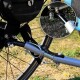 Nahaufnahme eines Fahrradanhängers mit einem schwarzen Riemen, einer silbernen Feder, Metallverbindern und einem kreisförmigen Ausschnitt detaillierter Komponenten.