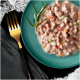 Une assiette teal avec de la nourriture humide pour animaux, de la viande hachée, des légumes colorés, une branche de romarin, une fourchette dorée et une serviette noire.