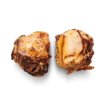 Zwei Hundekau-Knochen mit einer knusprigen Textur, einer zeigt einen Querschnitt, der den Knochen im Inneren offenbart, auf einem schwarzen Hintergrund.