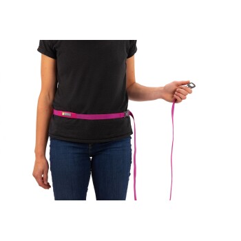 Eine Person in einem schwarzen T-Shirt hält eine pinke Hundeleine, die an einem passenden Gürtel befestigt ist, und zeigt eine freihändige Hundespazierlösung.