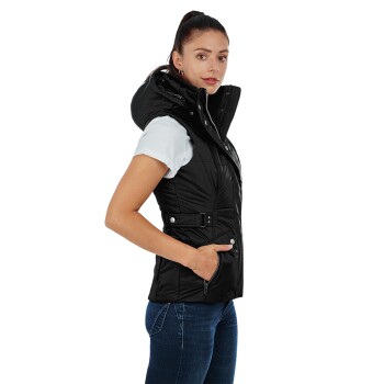 Eine Frau in einer schwarzen, gepolsterten Weste mit Kapuze, die seitlich steht mit der Hand in der Tasche, kombiniert mit einem weißen T-Shirt und blauen Jeans.