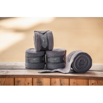 Vier gerollte graue Pferdebinden mit dem Etikett "EQUINATE", die auf einer Holzoberfläche angezeigt werden, mit einem verschwommenen Hintergrund.