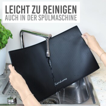 Eine Person hält eine schwarze Haustierpflegeunterlage unter fließendem Wasser in einem Waschbecken, mit dem Text "LEICHT ZU REINIGEN AUCH IN DER SPÜLMASCHINE" darüber.