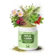 Ein Glas PfotenKraut "SOLE LUNA" Hundekräutermischung, aus dem Blumen, Kräuter und Samen herausspringen; Etikett lautet "Abwehr Kräuter für Hunde"