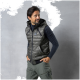 Eine Person, die eine grüne Steppweste mit Kapuze und ein navyblaues Langarmshirt trägt, steht vor einem grauen Hintergrund.