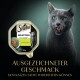 Eine graue Katze leckt sich die Lippen neben einer Sheba Katzenfutterpackung mit der Aufschrift "Selection in Sauce mit Kaninchen."