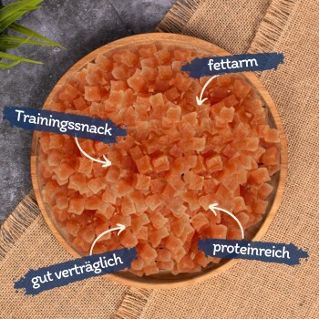 Eine Holzschüssel gefüllt mit kleinen, orangefarbenen Trainingssnacks für Haustiere, beschriftet mit Text, der angibt, dass sie fettarm, proteinreich und gut verträglich sind.