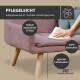 Ein rosa Sofa mit zwei türkisfarbenen Kissen steht auf einem Holzboden, begleitet von einem schwarzen Stuhl und einer pflanzenmotivierten Wandkunst darüber.