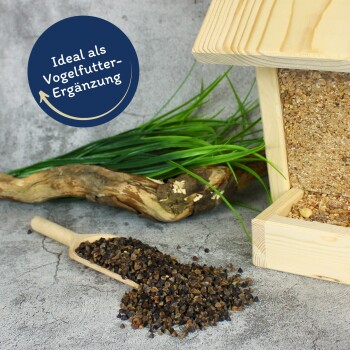 Vogelfutter, das auf einer Oberfläche verstreut ist, mit einer Holzschaufel, einem Vogelhaus im Hintergrund und einer Sprechblase mit dem Text 'Ideal als Vogelfutter-Ergänzung.'