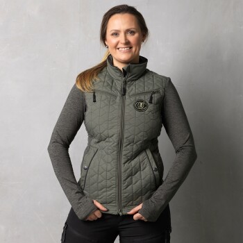 Eine Frau trägt eine stilvolle grüne gesteppte Weste mit einem Logo, kombiniert mit einem grauen Langarmoberteil, vor einem neutralen Hintergrund.