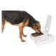 Ein Hund mit einem schwarz-braunen Fell frisst aus einem modernen weißen Haustierfutterspender mit offenem Deckel, der trockenes Futter zeigt.