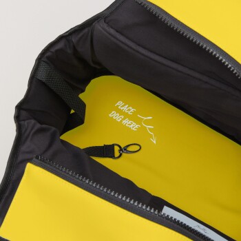 Eine Nahaufnahme des Innenraums eines gelben Haustierträgers, mit einem schwarzen Futter und einem Etikett, das sagt "HUND HIER PLATZIEREN" mit einem Pfeil.