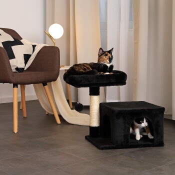 Gemütliches Wohnzimmer mit zwei Katzen: eine auf einem schwarzen Katzenbaum, die andere in einem Versteck. Ein brauner Stuhl und eine moderne Lampe vervollständigen die Szene.