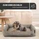 Ein Dackel mit einem grünen Halstuch entspannt sich in einem gemütlichen Hundebett auf einem Teppich, mit einem Holztisch in der Nähe. Text: "ZUM EINKUSCHELN."