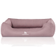 Ein weiches, mauvefarbenes Hundebett mit erhöhten Seiten und einem weißen "KNUFFELWUFF"-Logo auf der Vorderseite, das sich auf einer glänzenden Oberfläche spiegelt.