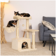 Zwei schildpattfarbene Katzen spielen und entspannen auf einem beigen Katzenbaum mit mehreren Ebenen und einem hängenden Spielzeug, neben einem grauen Sofa.